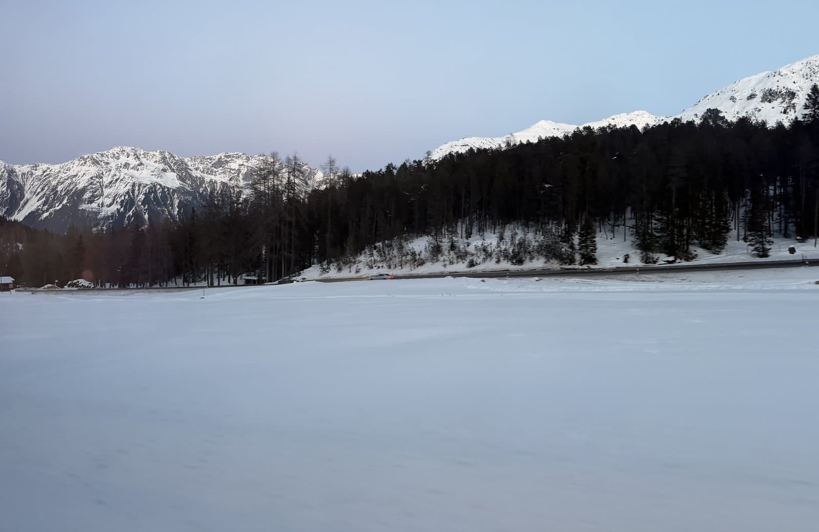 The frozen lake at Davos Wolfgang at dusk, with larch forest and snow-covered peaks behind, during the World Economic Forum Annual Meeting week, January 2026
